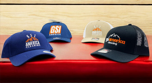 Assorted GSI America Cleaning branded caps in various styles and colors displayed on a red surface