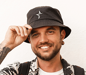 A man with a smily face is wearing a black bucket hat with a star logo on it.