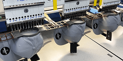 Multiple gray hats being embroidered in a production line.