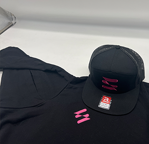 Black cap with pink logo beside a matching black hoodie on a white surface.