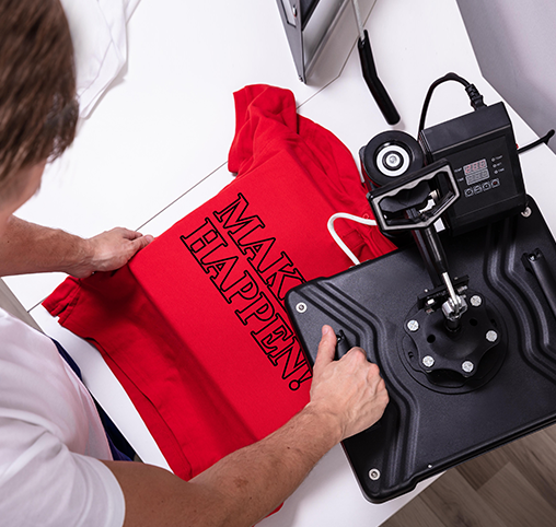 Person using a heat press machine on a red hoodie with the text "MAKE IT HAPPEN" in white.