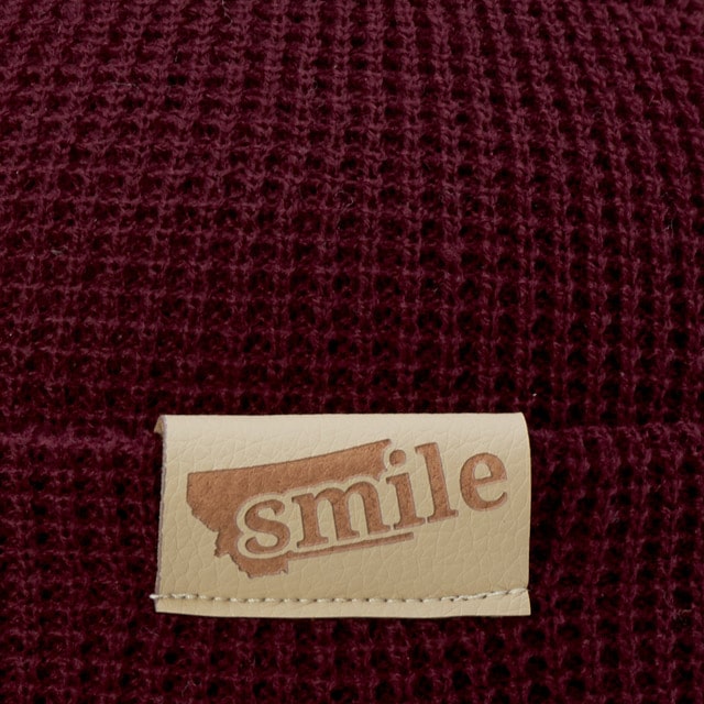 A burgundy knitted texture with a 'smile' leather patch label in lighter tone