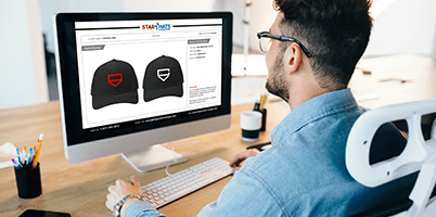 Person reviewing hat design mockups on a desktop computer.