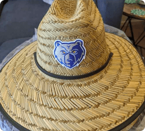 Straw hat with a bear logo patch on the front band, placed on a circular table.