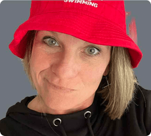 Woman smiling in a red bucket hat with _SWIMMING_ text on the front