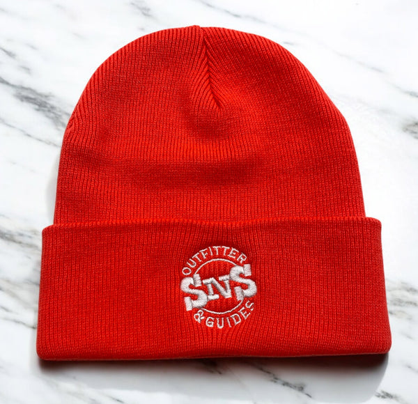 Bright red knit beanie with SNS Outfitter & Guides white embroidery on marble surface