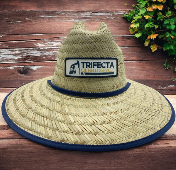 Straw hat with Trifecta Oil Field Services patch and blue trim on wooden background