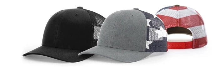 Three baseball caps in a row, from left to right: solid black, grey, and a red-white-blue pattern with a mesh back.