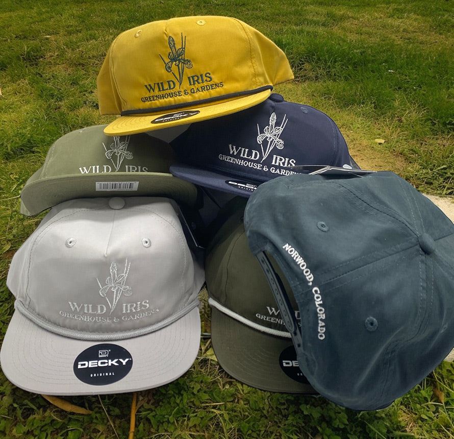 Assorted hats with 'Wild Iris Greenhouse & Gardens' logo in various colors.