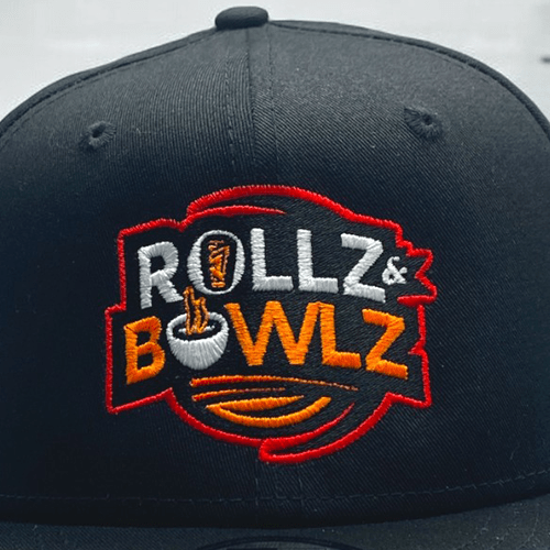 Black hat featuring a vibrant, custom flat embroidery design for 'Rollz & Bowlz' with bold red, white, and orange lettering and a food bowl graphic.