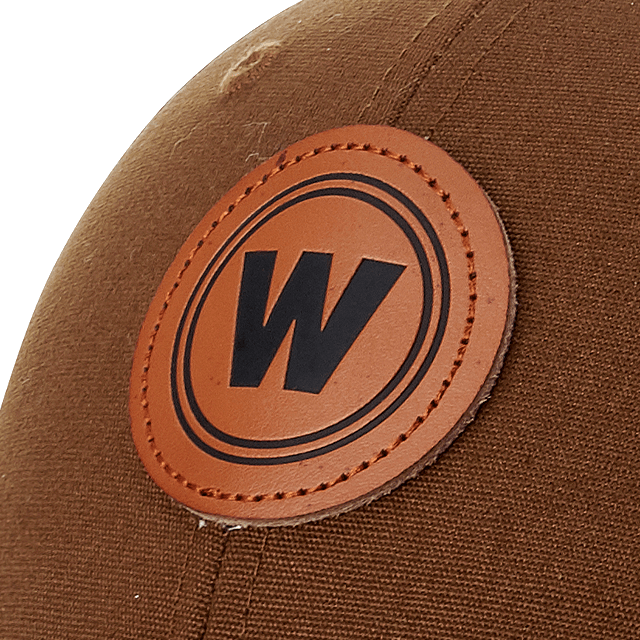 Close-up of a brown hat featuring a debossed leather patch with the letter "W" encircled in black on an orange background