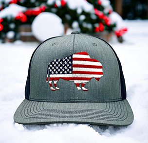 Dark grey cap with an American flag in buffalo silhouette on snowy background with red berries.
