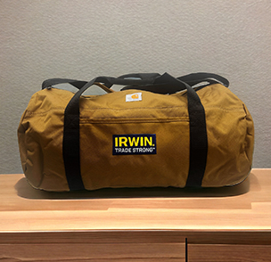 Yellow IRWIN duffel bag with black straps on a wooden shelf.