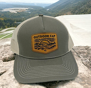 Gray and green cap with 'Outdoor Cap' mountain logo patch, displayed against a mountainous backdrop.