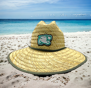 Straw beach hat with green bear logo patch on sandy beach with clear blue water in the background.