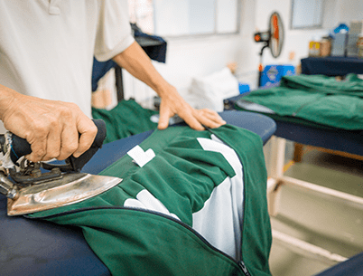 A worker ironing a green garment on an ironing board in a laundry facility.